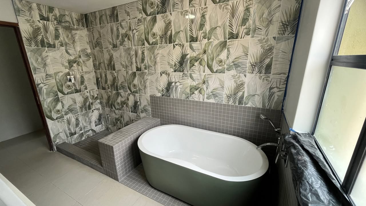 Botanical-themed bathroom with tropical leaf feature tiles, built-in tiled step and freestanding bathtub by Plumbing Beat