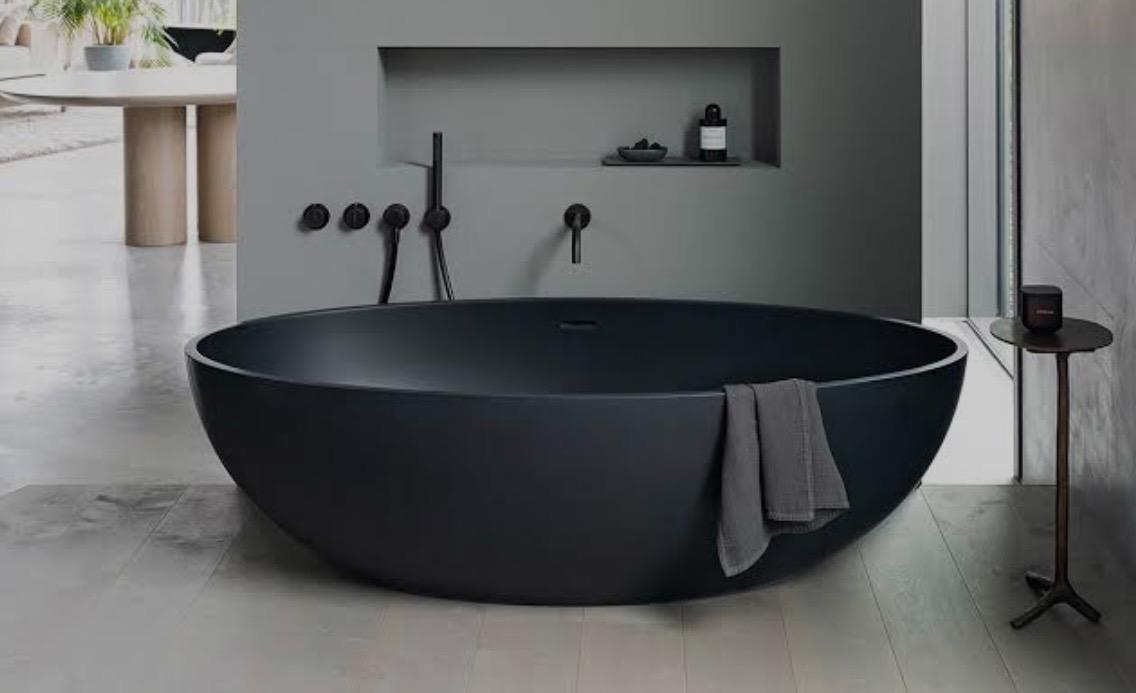 Designer matte black freestanding bathtub with black wall-mounted tapware in a minimalist grey bathroom