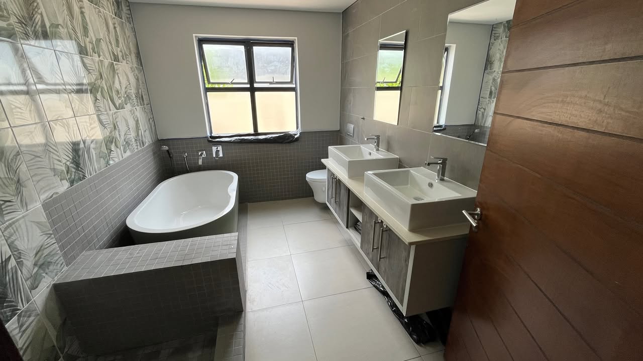 Complete bathroom renovation with botanical feature wall, freestanding bath on tiled plinth, double vessel basins and large mirror by Plumbing Beat