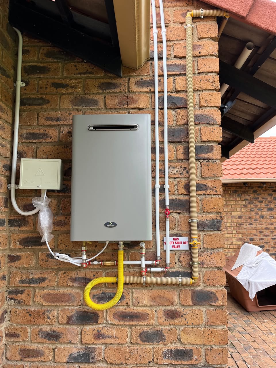 Wall-mounted Dewhot gas geyser installation with yellow gas flex piping, safety shut-off valve and copper water connections by Plumbing Beat