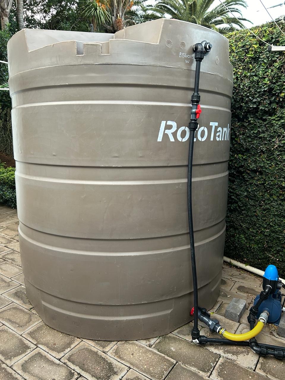Large RotoTank water storage tank with booster pump and piping connections installed at a residential property by Plumbing Beat